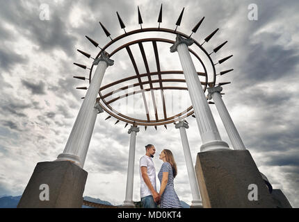 Glückliches Paar in der Holding durch die Hände im Haus mit Dach in Form von Shanyrak - den kasachischen Symbol der Familie in der berühmten Park in Almaty, Kasachstan Stockfoto