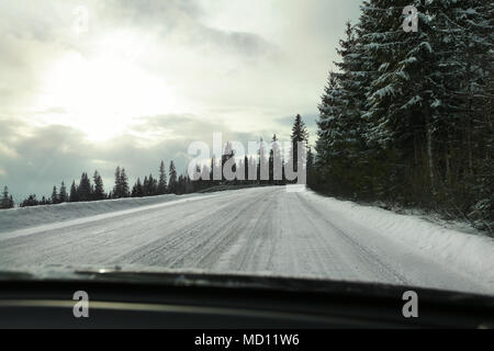 Blick vom Fahrersitz auf der Strasse mit Schnee bedeckt, starker blendende Sonne zurück Licht, riskante Fahrsituationen. Stockfoto
