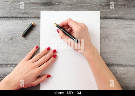 Blick von oben auf die Frau Hände mit roten Nägeln, Holding schwarz Brunnen Kugelschreiber mit Gold nib, bereit, etwas auf leeres Stück Papier zu schreiben zur Festlegung Stockfoto