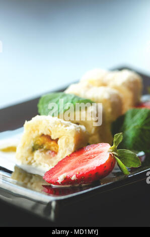 Weiße Brötchen mit Kiwi, Pfirsiche, Erdbeeren, Minze. Serverd mit Mandel Pfirsich- und Schokolade Saucen auf schwarzem Teller. Süße Nachspeise für Mädchen, Frau, Stockfoto