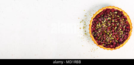 Süße Torte mit Himbeeren, Kirschen, rote Johannisbeeren mit Pistazien, Puderzucker auf Weiß konkreten Hintergrund. Copyspace. Ansicht von oben. Stockfoto