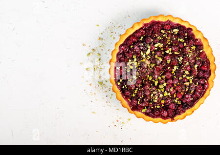 Süße Torte mit Himbeeren, Kirschen, rote Johannisbeeren mit Pistazien, Puderzucker auf Weiß konkreten Hintergrund. Copyspace. Ansicht von oben. Stockfoto