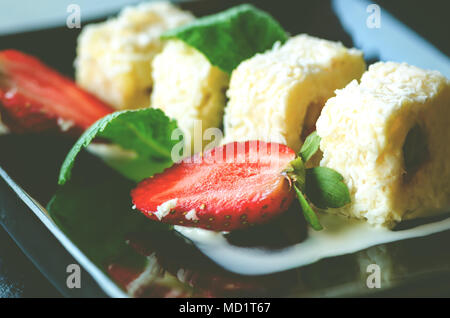 Weiße Brötchen mit Kiwi, Pfirsiche, Erdbeeren, Minze. Serverd mit Mandel Pfirsich- und Schokolade Soßen auf schwarze Platte Stockfoto