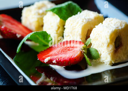 Weiße Brötchen mit Kiwi, Pfirsiche, Erdbeeren, Minze. Serverd mit Mandel Pfirsich- und Schokolade Soßen auf schwarze Platte Stockfoto