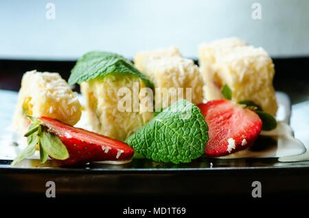 Weiße Brötchen mit Kiwi, Pfirsiche, Erdbeeren, Minze. Serverd mit Mandel Pfirsich- und Schokolade Soßen auf schwarze Platte Stockfoto