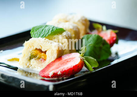 Weiße Brötchen mit Kiwi, Pfirsiche, Erdbeeren, Minze. Serverd mit Mandel Pfirsich- und Schokolade Soßen auf schwarze Platte Stockfoto