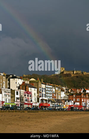 Ein Regenbogen über Scarborough Castle. Winter Sonnenschein und Duschen verbinden sich zu einem bunten Regenbogen über der Burg der Stadt und South Bay Seafront zu produzieren. Stockfoto