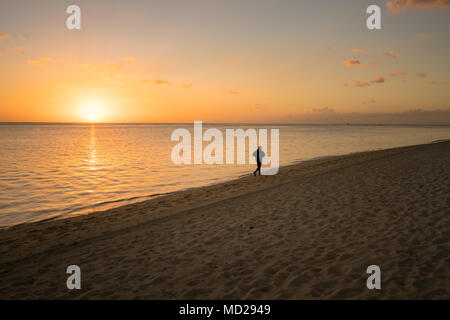 Eine Silhouette läuft allein am Strand bei Sonnenuntergang auf Mauritius. Stockfoto