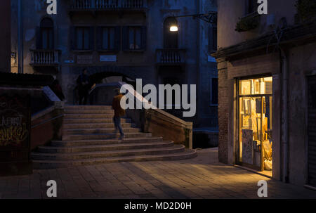 Ein Fußgänger geht über eine Kanalbrücke in der Calle de Mezo im Stadtteil Santa Croce von Venedig, Italien. Stockfoto