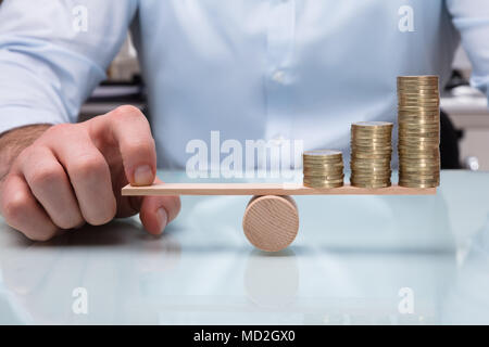 Nahaufnahme einer Businessperson Balancing erhöht Gestapelte Münzen mit Finger auf Wippe Stockfoto