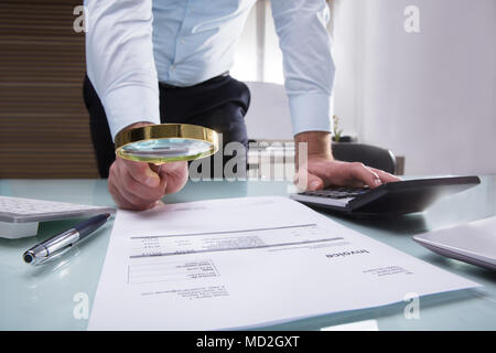 Nahaufnahme der Kaufmann Hand mit Lupe über Rechnung am Arbeitsplatz Stockfoto