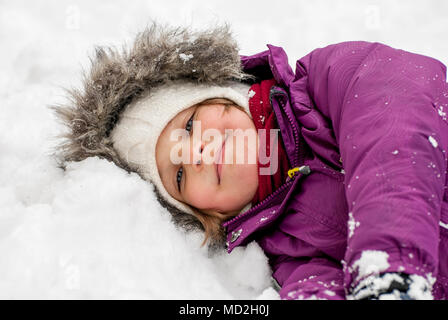 Müde, kleines Mädchen, die Verlegung in den Schnee und lächelnd. Stockfoto