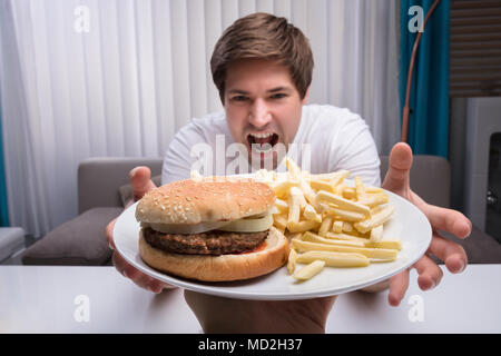 Mann unter Junk Food auf der Platte, die durch eine Person Stockfoto