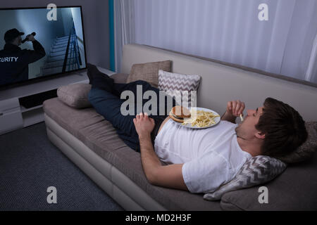 Junger Mann auf dem Sofa liegend Essen Pommes und Burger Stockfoto