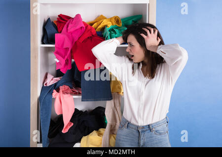Nahaufnahme einer schockiert junge Frau Vor unordentlicher Kleidung im Regal Stockfoto