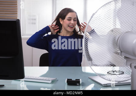 Lächelnden jungen Geschäftsfrau kühlen sich mit elektrischen Ventilator bei heißem Wetter Stockfoto