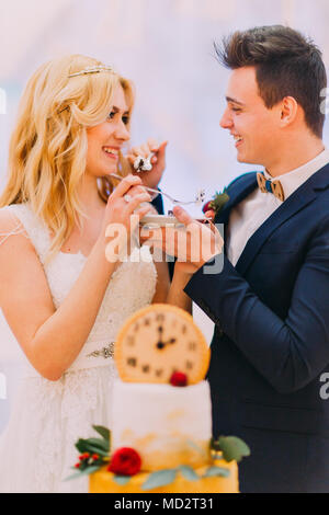 Hübscher Bräutigam seine schönen blonden Braut Fütterung mit Hochzeitstorte Stockfoto