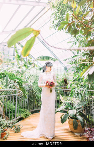 Fröhliche Braut mit der wed-Bouquet ist neben der Suche und genießen die Zeit im Gewächshaus. Stockfoto