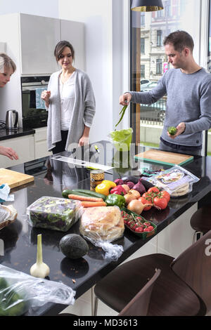 Mann hilft in der Küche. Gruppe von Freunden beiläufig auf eine Auswahl an Essen naschen beim Lachen und sich zu amüsieren. Stockfoto