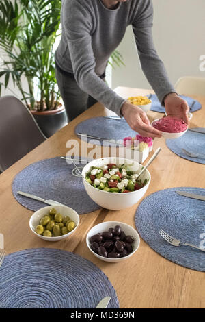 Einrichten der Tabelle für vegtarian Mahlzeit - griechischer Salat, grüne und schwarze Oliven und Rote Beete Hummus - selektive Fokus Stockfoto