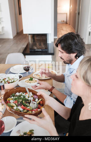 Gruppe von Freunden beiläufig Snacking auf eine Auswahl von Lebensmitteln beim Lachen und sich zu amüsieren. Mit gebratenem Gemüse-selektiven Fokus Stockfoto