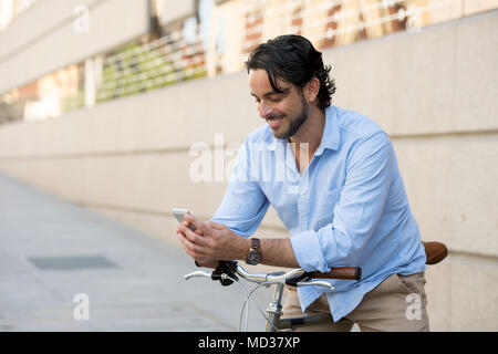 Junge glücklich attraktive Hispanic Mann in ungezwungener trendige Kleidung lächelt fröhlich mit Handy auf vintage Coole Retro Fahrrad in moderner, stilvoller lifes Stockfoto