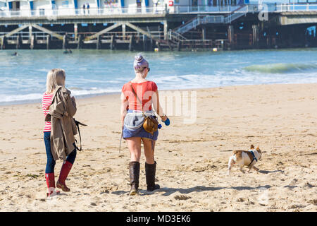 Bournemouth, Dorset, Großbritannien. 18. April 2018. UK Wetter: schön warmen sonnigen Tag in Bournemouth Stränden mit klarem blauen Himmel und Sonnenschein, ungebrochen als Besucher der seaside Leiter der wärmste Tag des Jahres so weit zu genießen. Zwei junge Frau zu Fuß Hund an der Küste entlang. Mini Hitzewelle. Credit: Carolyn Jenkins/Alamy leben Nachrichten Stockfoto