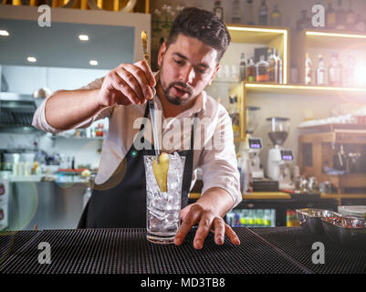 Barkeeper in einem weißen Hemd und schwarze Schürze, Hinzufügen einer Scheibe Ingwer in ein Glas Stockfoto