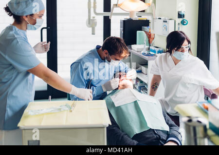 Zahnarzt in den Mund der männlichen Patienten suchen, zahnmedizinische Krankenschwestern Ausrüstung vorbereiten Stockfoto
