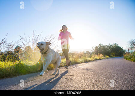 Junge Frau entlang der Landstraße laufen mit Hund, Low Angle View Stockfoto