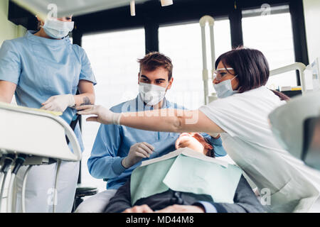 Zahnarzt in den Mund der männlichen Patienten suchen, zahnmedizinische Krankenschwestern Ausrüstung vorbereiten Stockfoto