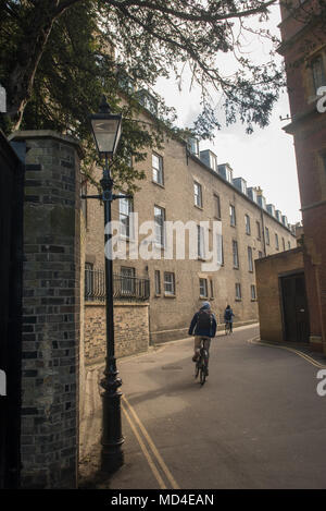 Person spaziert durch eine enge Gasse in Cambridge, Großbritannien, gesäumt von historischen Universitätsgebäuden und Kopfsteinpflastersteinen an einem hellen, klaren Tag Stockfoto
