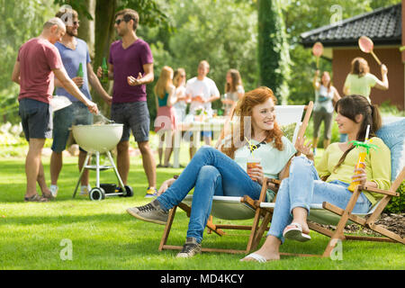 Zwei attraktive Frauen auf einer Gartenparty chatten mit vielen Freunden grillen, spielen, Badminton, und Essen Stockfoto