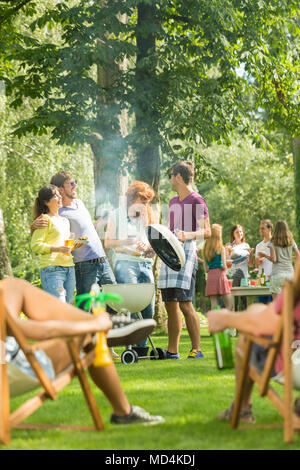 Grill Party in einem Park von einer großen Gruppe von Freunden genießen das warme Wetter und Essen statt Stockfoto