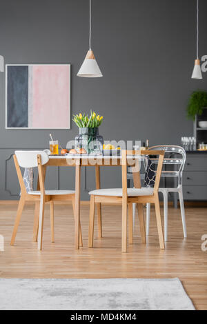 Creative Design moderne Stühle um eine einfache Küche Tisch mit Tischdecke in einem grauen Raum apartment Innenraum Stockfoto