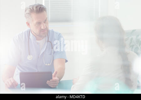 Schwere Arzt diskutieren eine Krankheit mit seinen Patienten im Krankenhaus Stockfoto