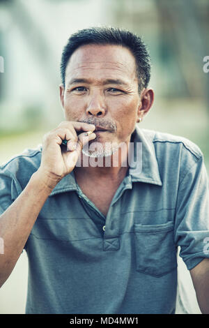 Nahaufnahme Gesicht des asiatischen älterer Mann mit trockenen Blättern Zigarette zu Kamera suchen Stockfoto