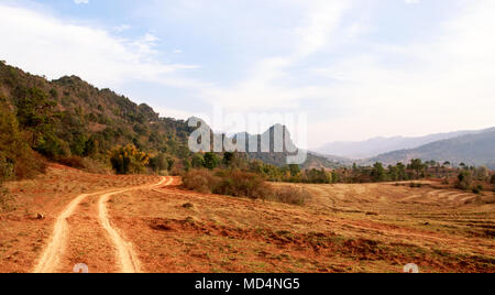 Dirt Road Wind zwischen trockenen Ackerland und Mittelgebirge im Shan Staat, Myanmar Stockfoto