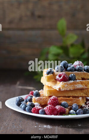 Leckere süße Waffeln mit Himbeeren und Blaubeeren auf einem alten Holztisch. Stockfoto