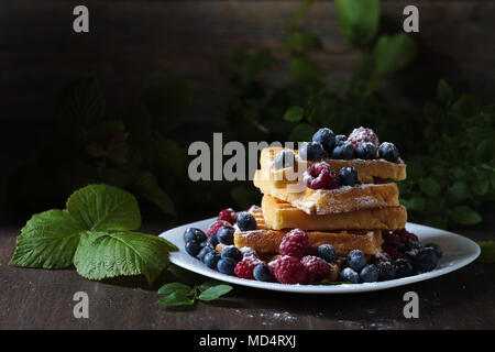 Leckere süße Waffeln mit Himbeeren und Blaubeeren auf einem alten Holztisch. Stockfoto