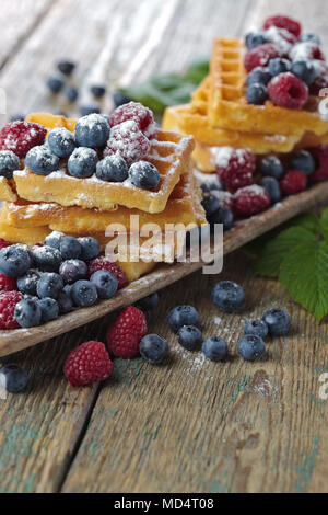 Leckere süße Waffeln mit Himbeeren und Blaubeeren auf einem alten Holztisch. Stockfoto