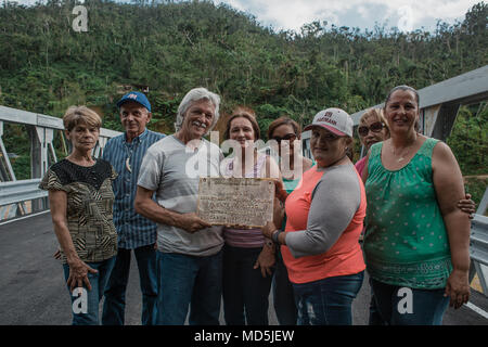 Utuado, Puerto Rico. März 13, 2018 -- Überlebenden Posieren vor der neuen Brücke und der Widmung Plakette der vorherigen zeigen. Diese Menschen unter vielen anderen Familien wurden durch den Zusammenbruch der früheren Brücke nach Hurrikan María durch die Insel am 20. September 2017 Rissen betroffen. Heute, dank der Bemühungen der staatlichen, lokalen und föderalen Agenturen, hat die Gemeinschaft eine neue Brücke. Die FEMA/Eduardo Martínez Stockfoto