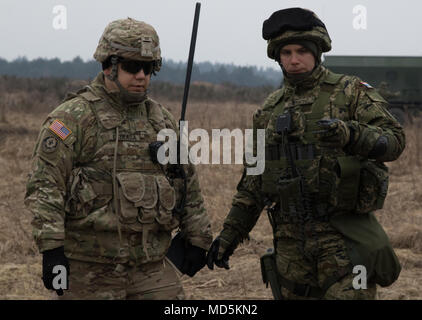 Eine kroatische Artillerie Soldaten zugeordnet Vulkan Batterie (rechts) erklärt der US-Armee Maj. Jakob Estrada (links), Operations Officer der Feldartillerie Geschwader zugewiesen sind, 2.Kavallerie Regiments, wie viele Runden wird aus dem Vulkan M-92 abgefeuert werden, Mobile Mehrere Raketenwerfer, während der Akku im 3. Staffel teilnimmt, 2. Reiterregiment, Squadron live fire Übung in einem Bereich in der Nähe der Bemowo Piskie, Polen, 23. März 2018. Diese Soldaten sind ein Teil der einzigartigen, multinationalen Battle Group aus USA, Großbritannien, Kroatischen und rumänischen Soldaten, die mit dem Pol dienen Stockfoto