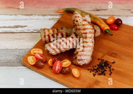 Fertig gegrillte Steaks saftige Teile mit Tomaten und Gemüse auf einem alten Holzbrett serviert. Stockfoto