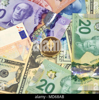 MONTREAL, KANADA - 10. MÄRZ 2018: astraleums cryptocurrency gold coin und Logo auf Euro, US-Dollar, kanadische Dollar Banknoten. Stockfoto