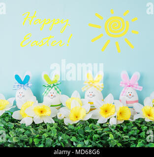 Einige lustige Osterhasen mit bunten Bögen von Ostern Eier, die von Gras, Blumen und der Sonne umgeben, mit der Aufschrift Frohe Ostern! Stockfoto