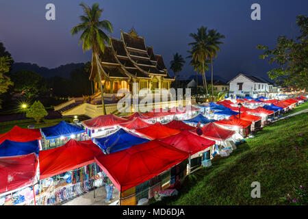 Night Market und beleuchtete Haw Pha Bang Tempel, auch als Royal oder Schlosskapelle, neben dem königlichen Palast in Luang Prabang, Laos bekannt, in der Dämmerung. Stockfoto