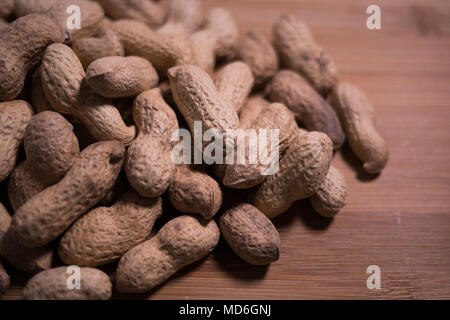 Stapel von natürlichen schale Erdnüsse in der Schale auf einem hölzernen genarbt Hintergrund und natürliches Licht und Schatten. Stockfoto