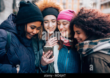 Vier junge Frauen multiethnischen Outdoor mit smart phone Outdoor - lächelnd, soziales Netzwerk, Kommunikation Konzept Stockfoto