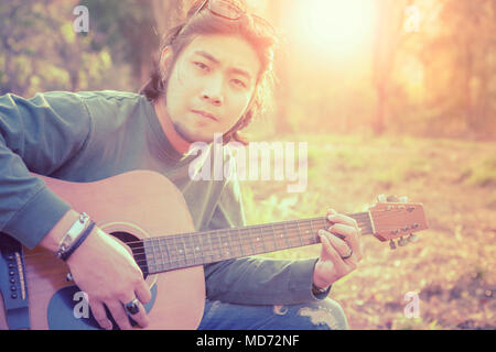 Asiatische freischaffender Musiker spielen Folk Guitar outdoor gegen schöne Sonne Licht Stockfoto